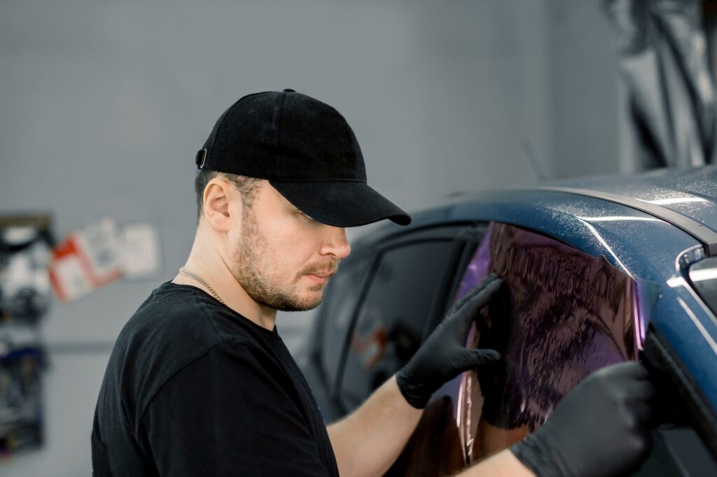 Professional car service worker tinting a car window with tinted foil